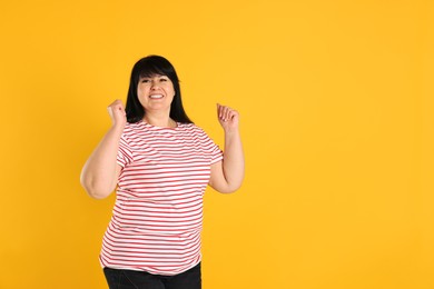 Happy overweight mature woman on orange background, space for text