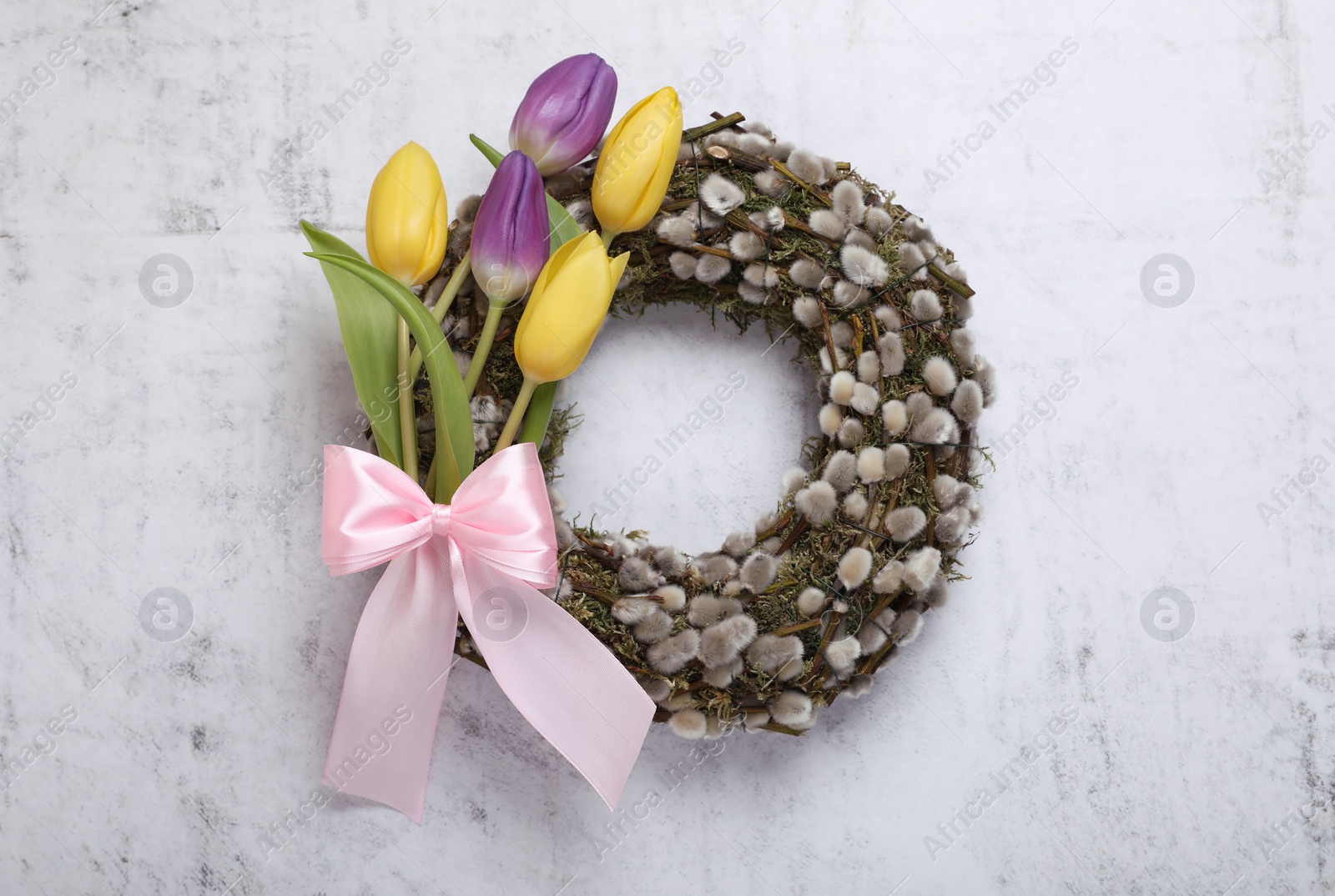 Photo of Wreath made of beautiful willow, colorful tulip flowers and pink bow on light background, top view