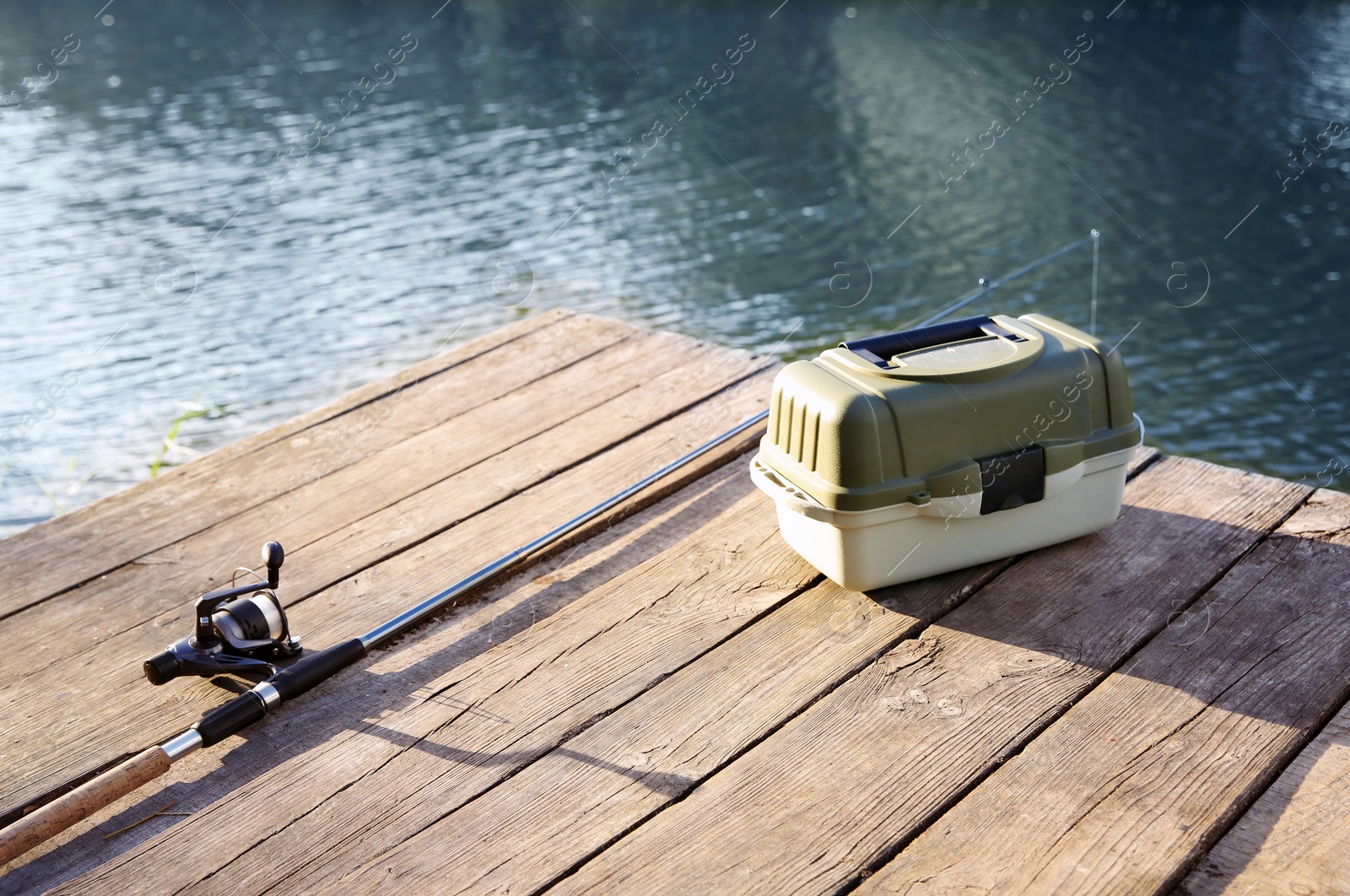 Photo of Tackle box and rod for fishing on wooden pier at riverside. Recreational activity