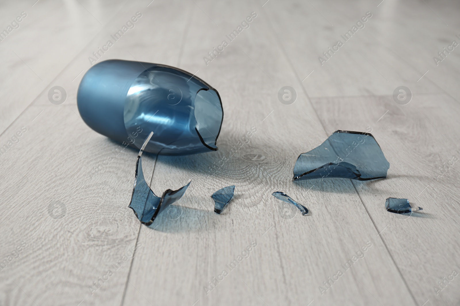 Photo of Broken blue glass vase on wooden floor, closeup