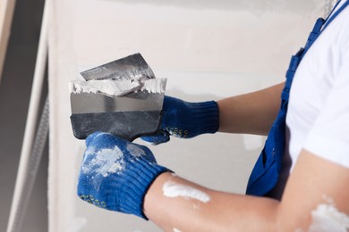 Photo of Worker with putty knives and plaster near wall indoors, closeup. Home renovation