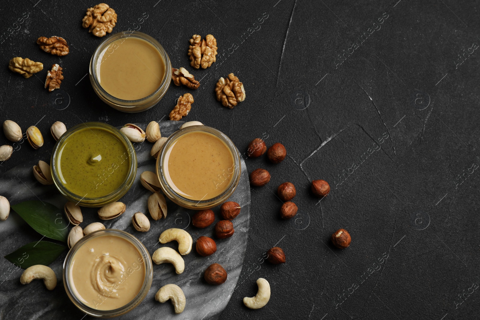 Photo of Jars with butters made of different nuts and ingredients on black table, flat lay. Space for text