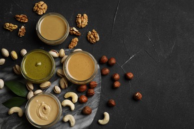 Photo of Jars with butters made of different nuts and ingredients on black table, flat lay. Space for text