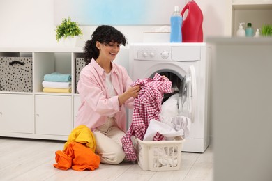 Happy woman with laundry near washing machine indoors