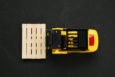 Toy forklift with wooden pallet on black table, top view