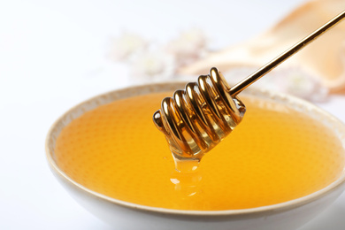 Photo of Bowl with organic honey and dipper on white background, closeup