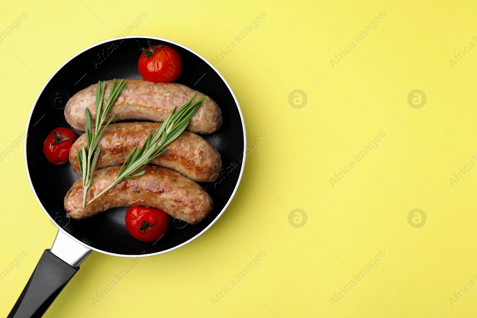 Photo of Frying pan with tasty homemade sausages, rosemary and tomatoes on yellow table, top view. Space for text