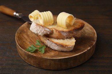 Photo of Tasty butter curls and slices of bread on wooden table, closeup