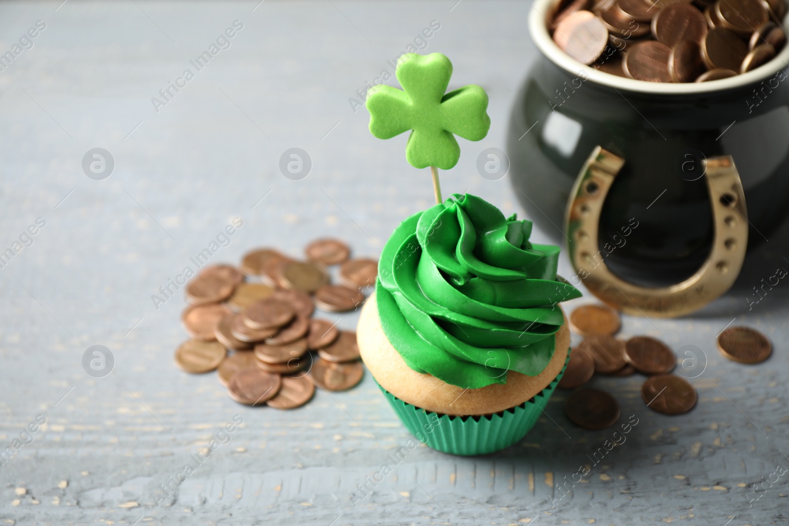 Photo of Decorated cupcake and pot with gold coins on grey wooden table. St. Patrick's Day celebration