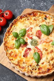 Tasty quiche with tomatoes, basil and cheese served on dark textured table, flat lay