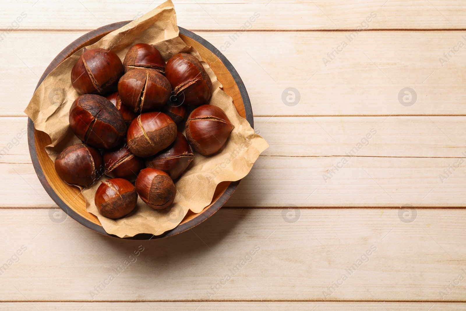 Photo of Roasted edible sweet chestnuts in bowl on wooden table, top view. Space for text