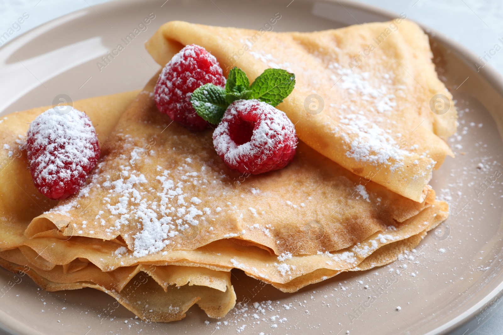 Photo of Delicious crepes served with mint, raspberries and powdered sugar on plate, closeup