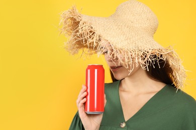 Woman in wicker hat holding red beverage can on yellow background