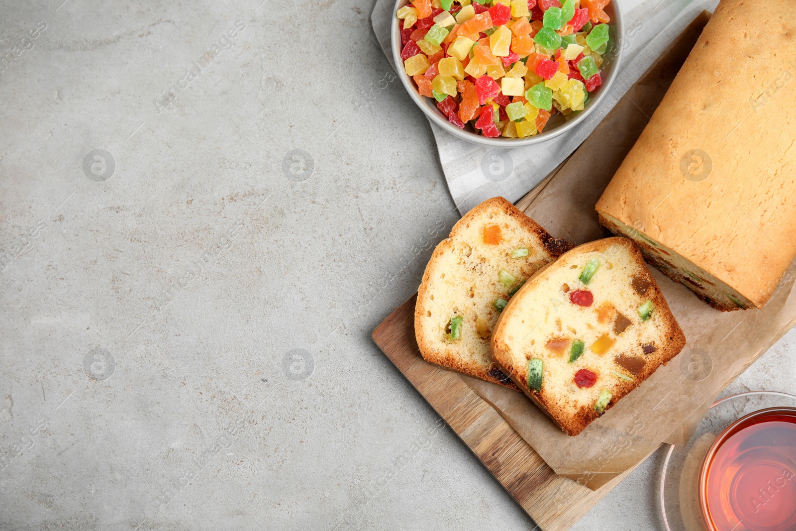 Photo of Delicious cake with candied fruits and tea on light grey table, flat lay. Space for text