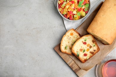 Photo of Delicious cake with candied fruits and tea on light grey table, flat lay. Space for text