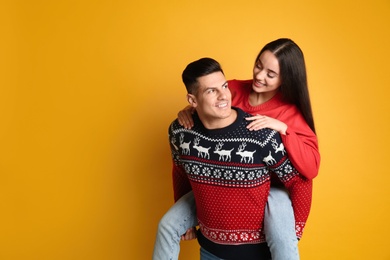 Photo of Couple in Christmas sweaters on yellow background, space for text