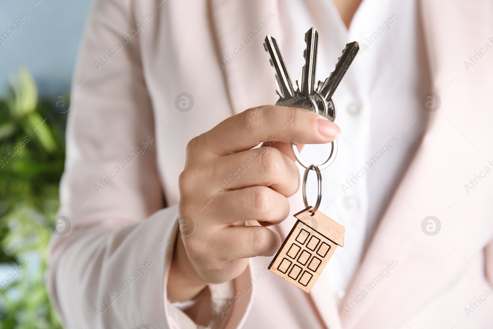 Photo of Woman holding bunch of house keys with trinket on blurred background, closeup