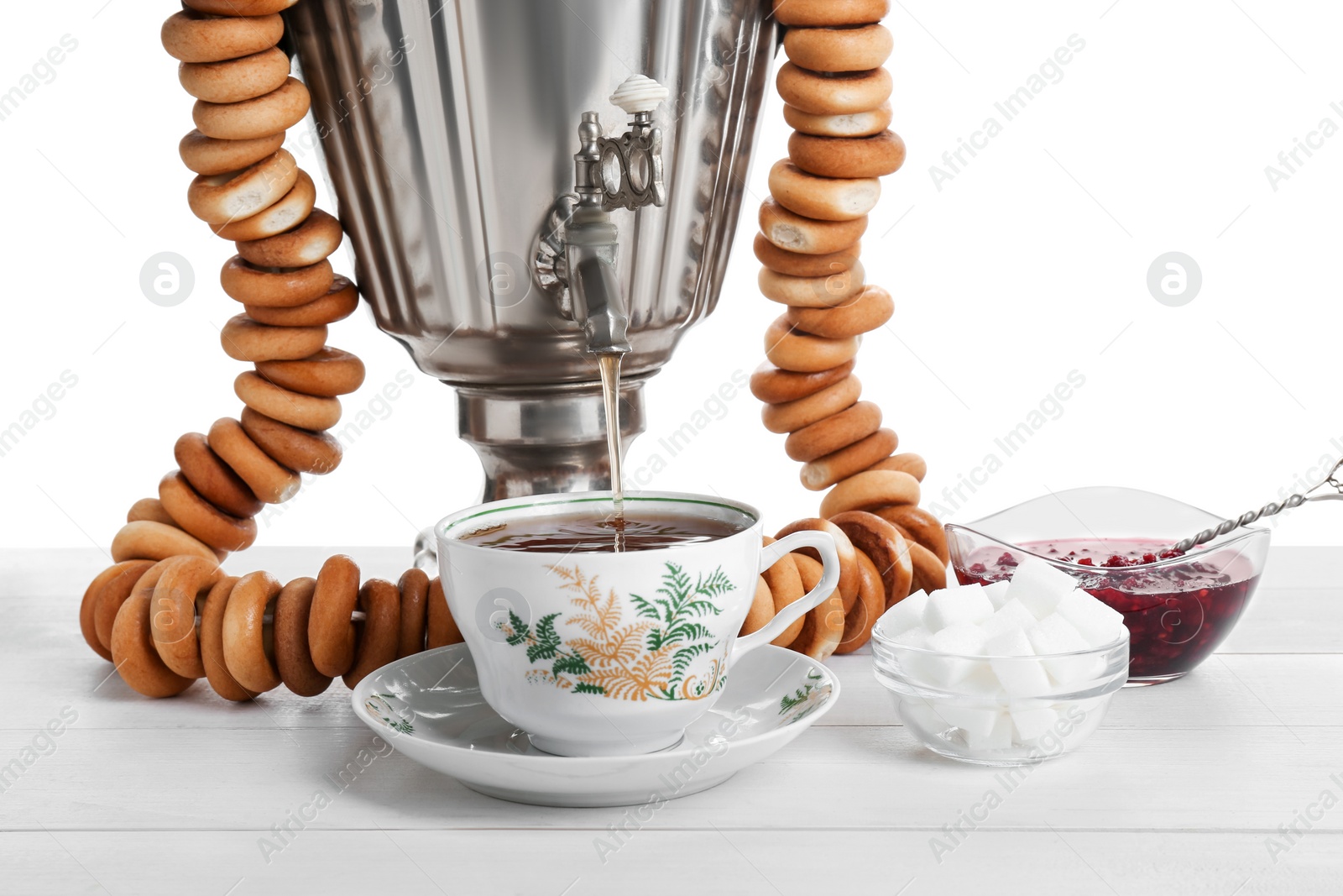 Photo of Samovar with hot tea, jam and delicious ring shaped Sushki (dry bagels) on table against white background