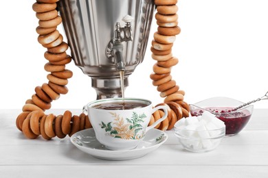 Samovar with hot tea, jam and delicious ring shaped Sushki (dry bagels) on table against white background