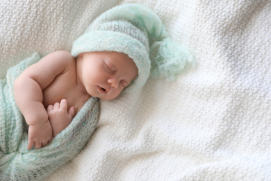 Photo of Cute newborn baby in warm hat sleeping on white plaid, above view. Space for text