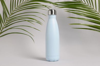 Photo of Stylish thermo bottle near tropical leaves on light grey background