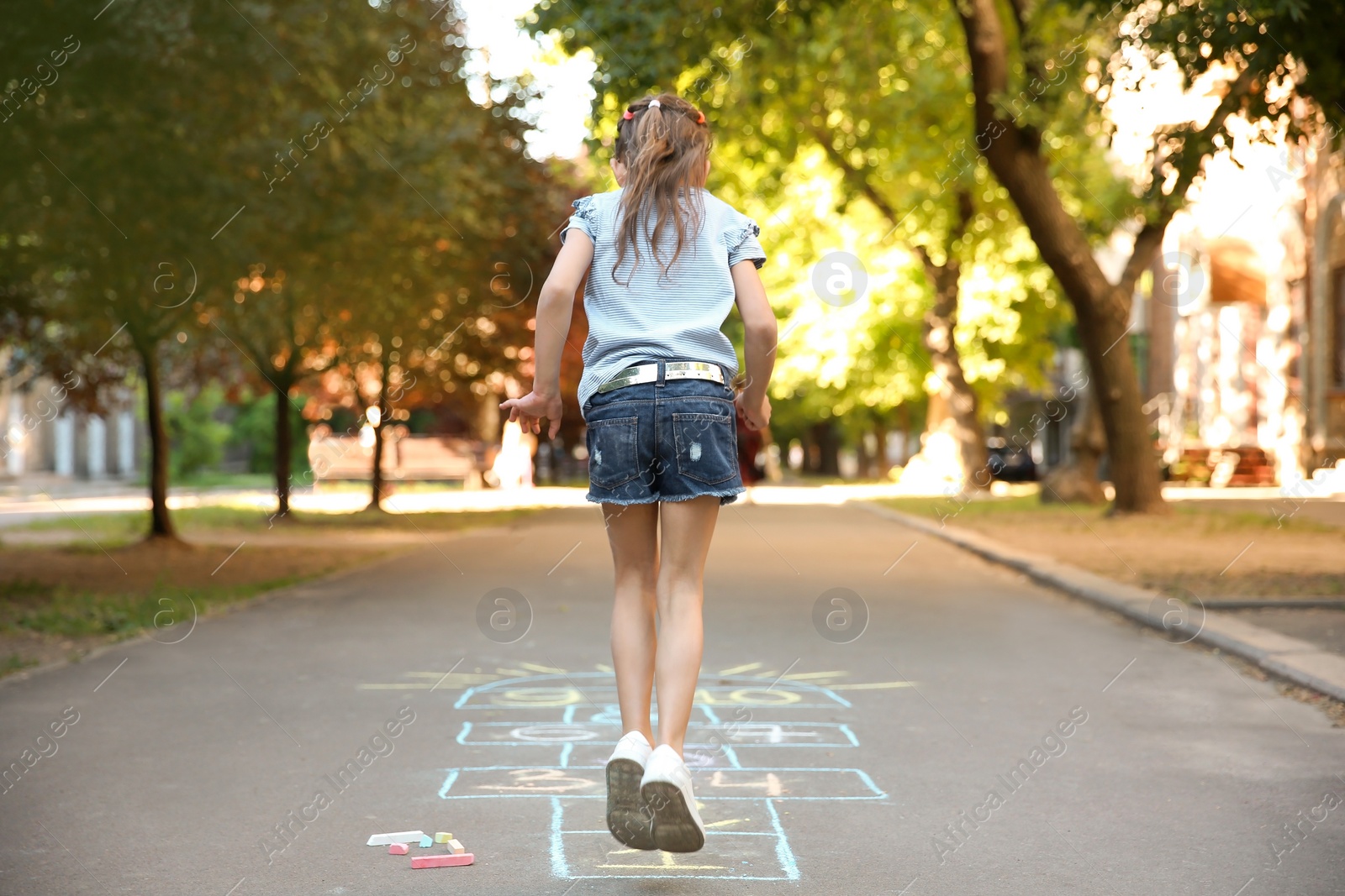 Photo of Little child playing hopscotch drawn with colorful chalk on asphalt