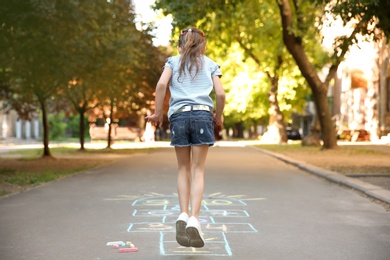 Little child playing hopscotch drawn with colorful chalk on asphalt