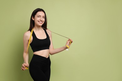 Photo of Happy young woman with measuring tape showing her slim body on green background, space for text