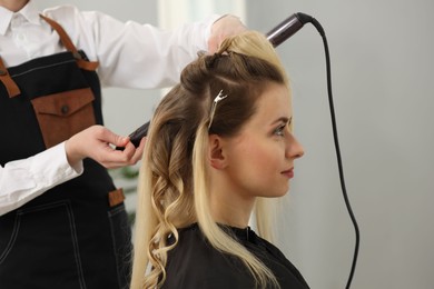 Hair styling. Hairdresser curling woman's hair in salon, closeup