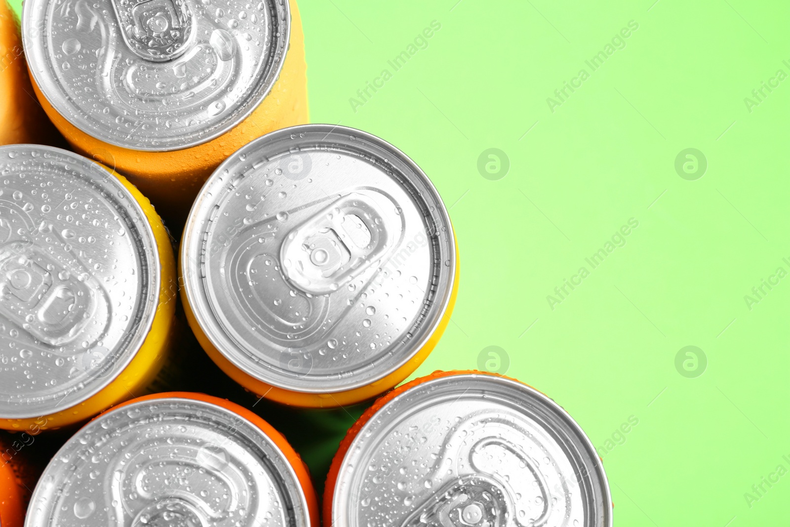 Photo of Energy drinks in wet cans on green background, top view. Space for text