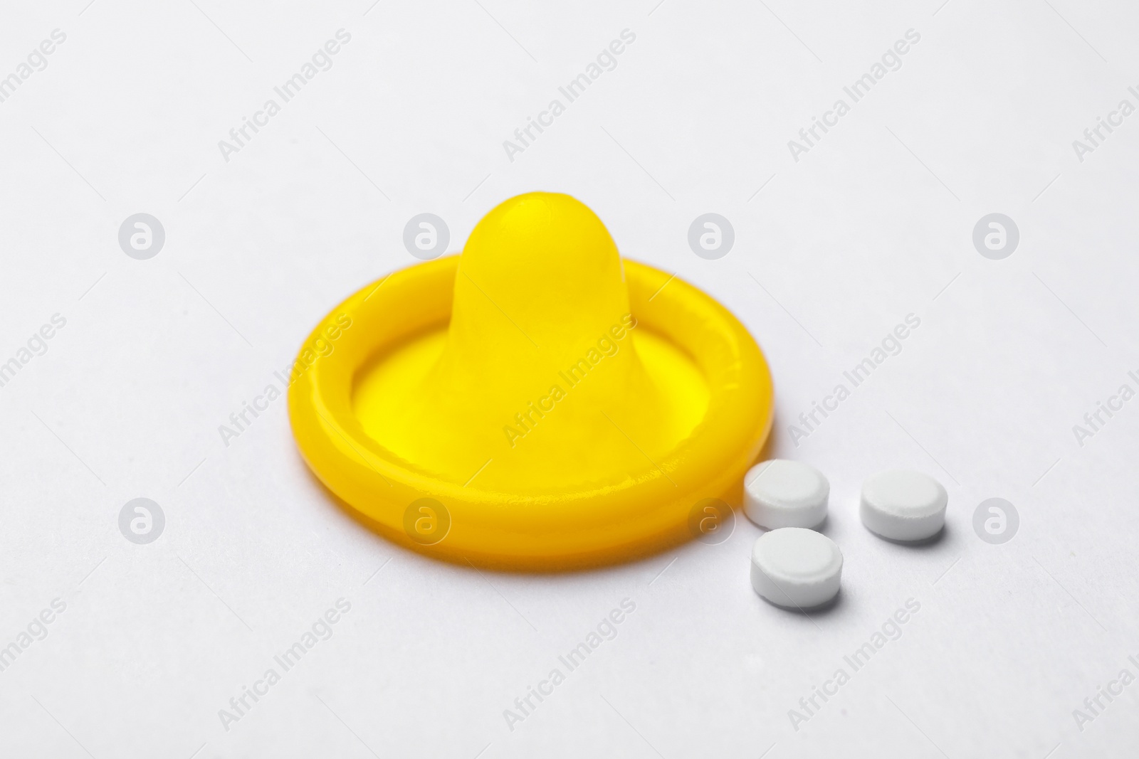 Photo of Yellow condom and birth control pills on white background. Safe sex concept