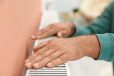 Photo of Man warming hands on heating radiator indoors, closeup