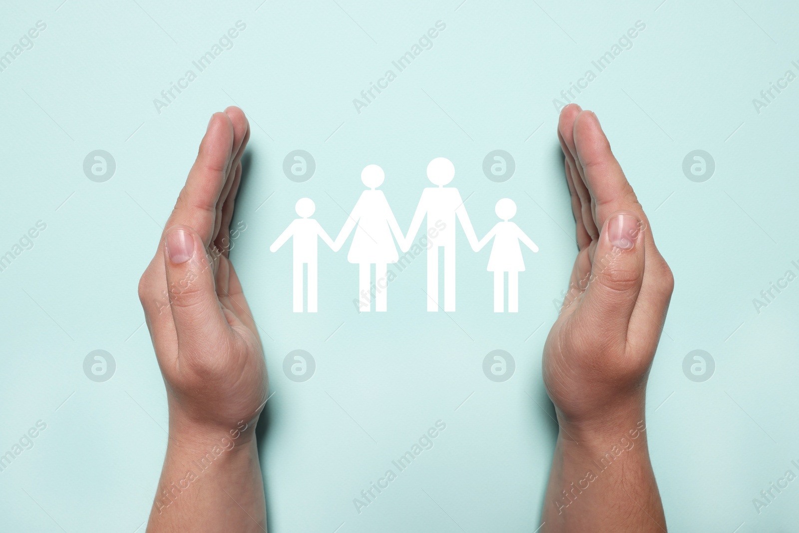 Image of Man holding hands around cutout paper silhouette of family on light blue background, top view. Insurance concept