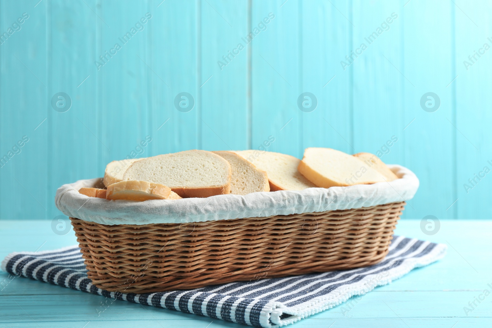 Photo of Slices of tasty fresh bread in wicker basket on light blue wooden table