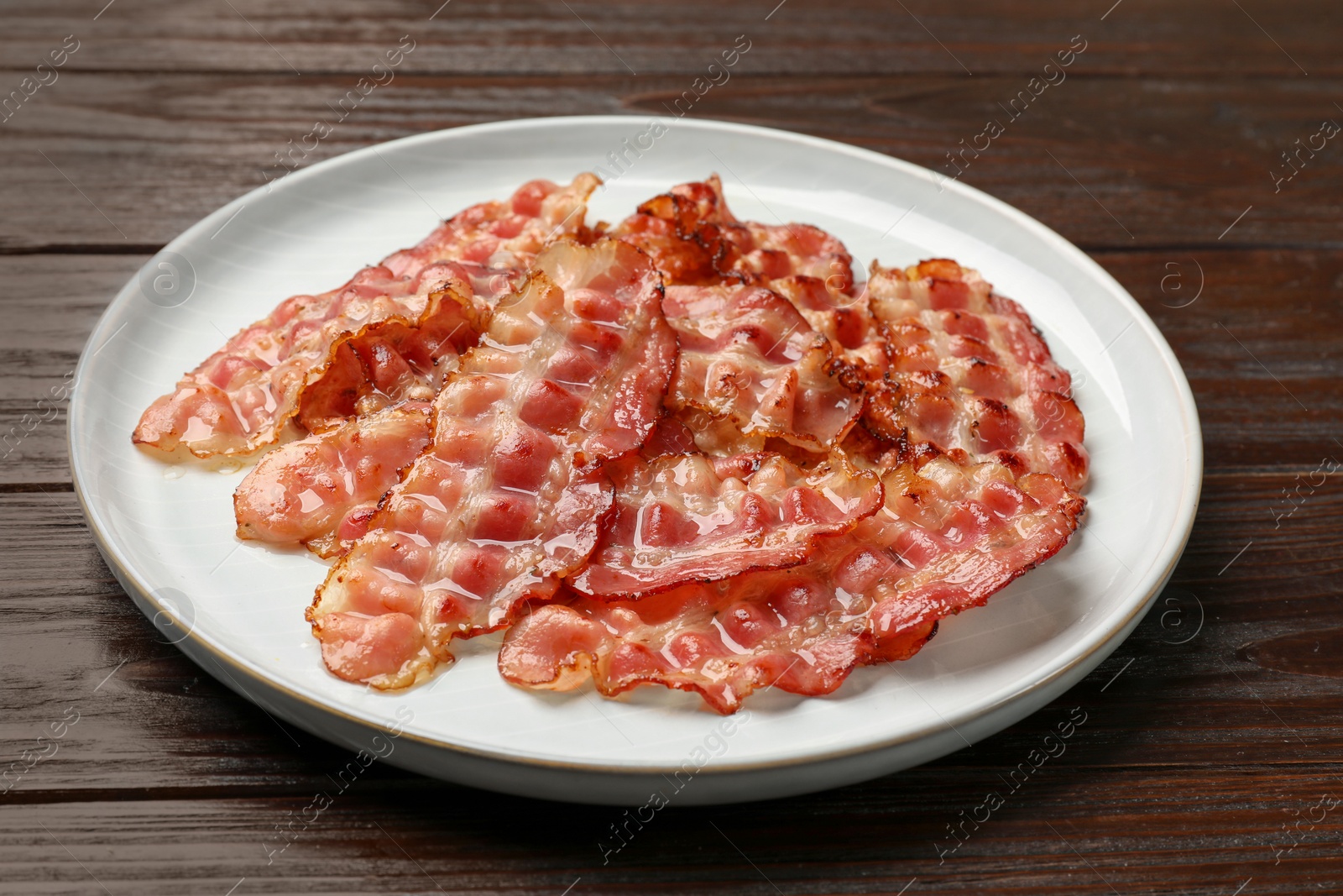 Photo of Plate with fried bacon slices on wooden table, closeup