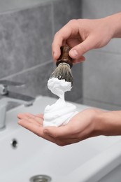 Photo of Man applying shaving foam onto brush in bathroom, closeup