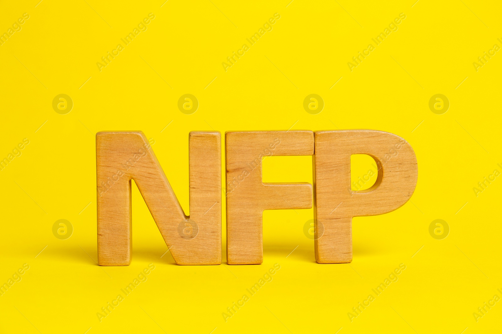 Photo of Wooden letters NFP on yellow background. Nonfarm payroll