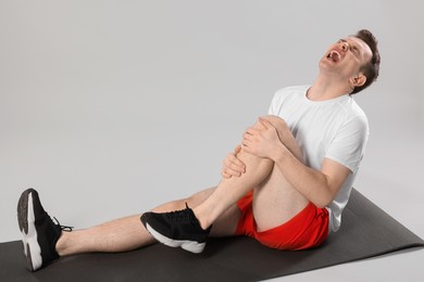 Photo of Man suffering from leg pain on mat against grey background