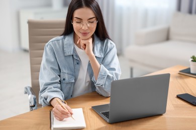 Young woman watching webinar at table in room