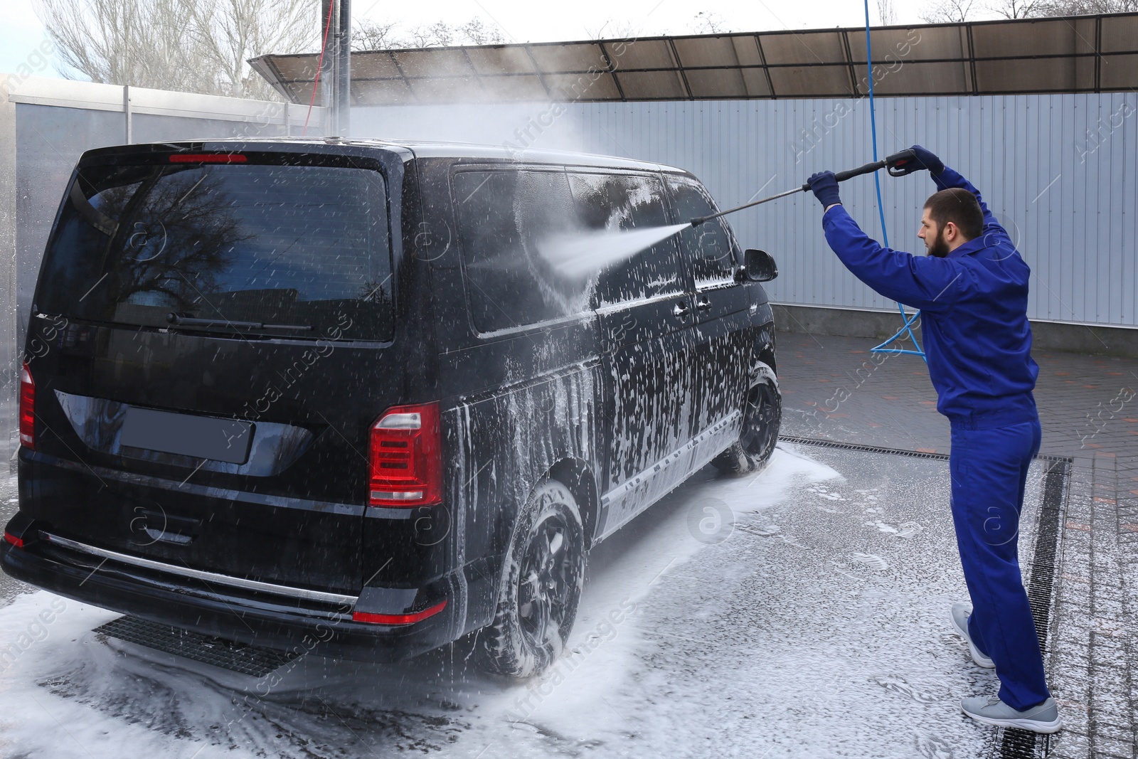 Photo of Worker cleaning automobile with high pressure water jet at car wash