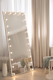 Large mirror with light bulbs near window in room. Interior design