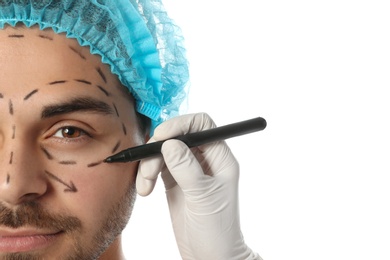 Doctor drawing marks on man's face for cosmetic surgery operation against white background, closeup