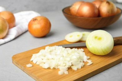 Wooden board with cut onion and knife on grey table