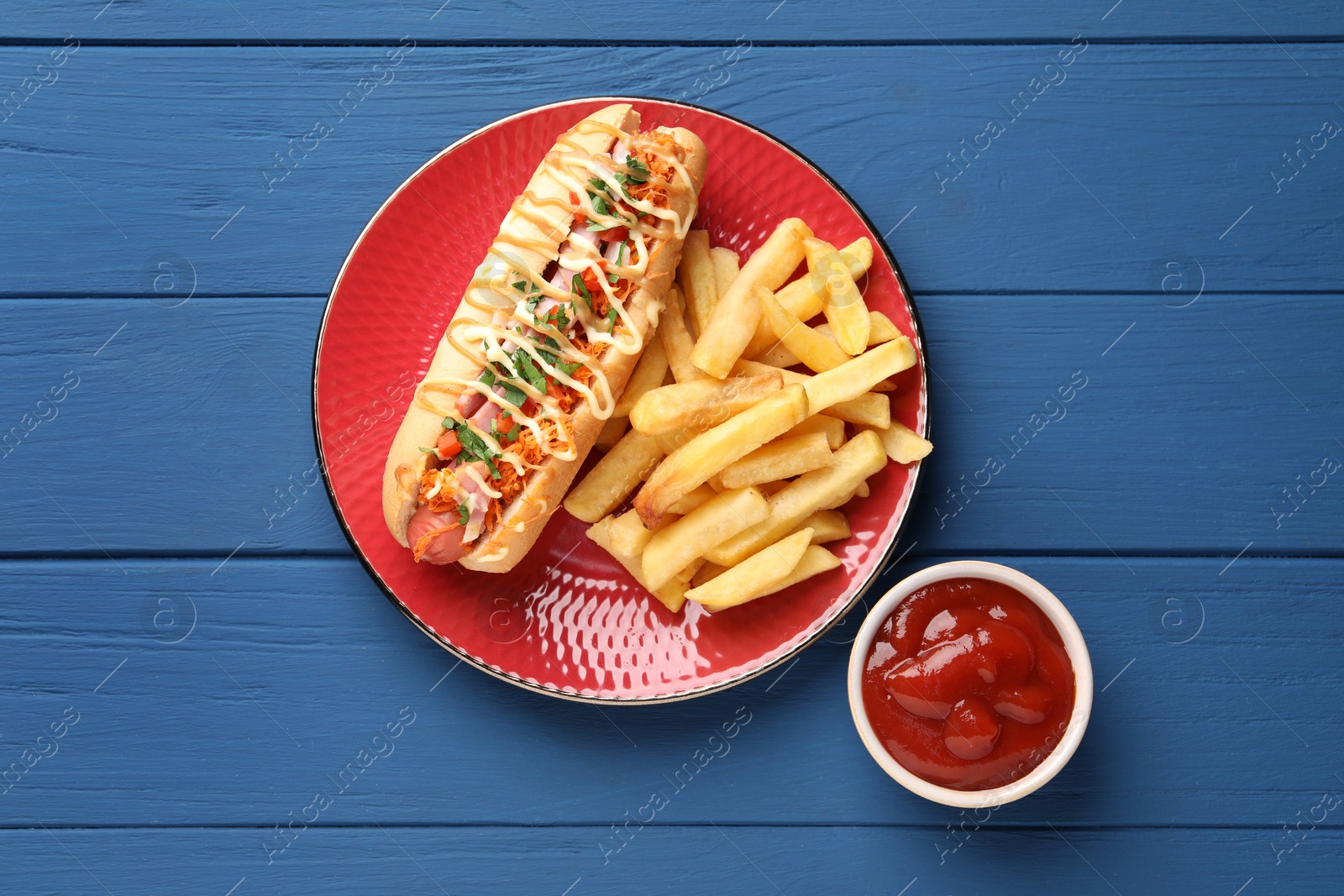 Photo of Delicious hot dog with bacon, carrot and parsley served on blue wooden table, flat lay