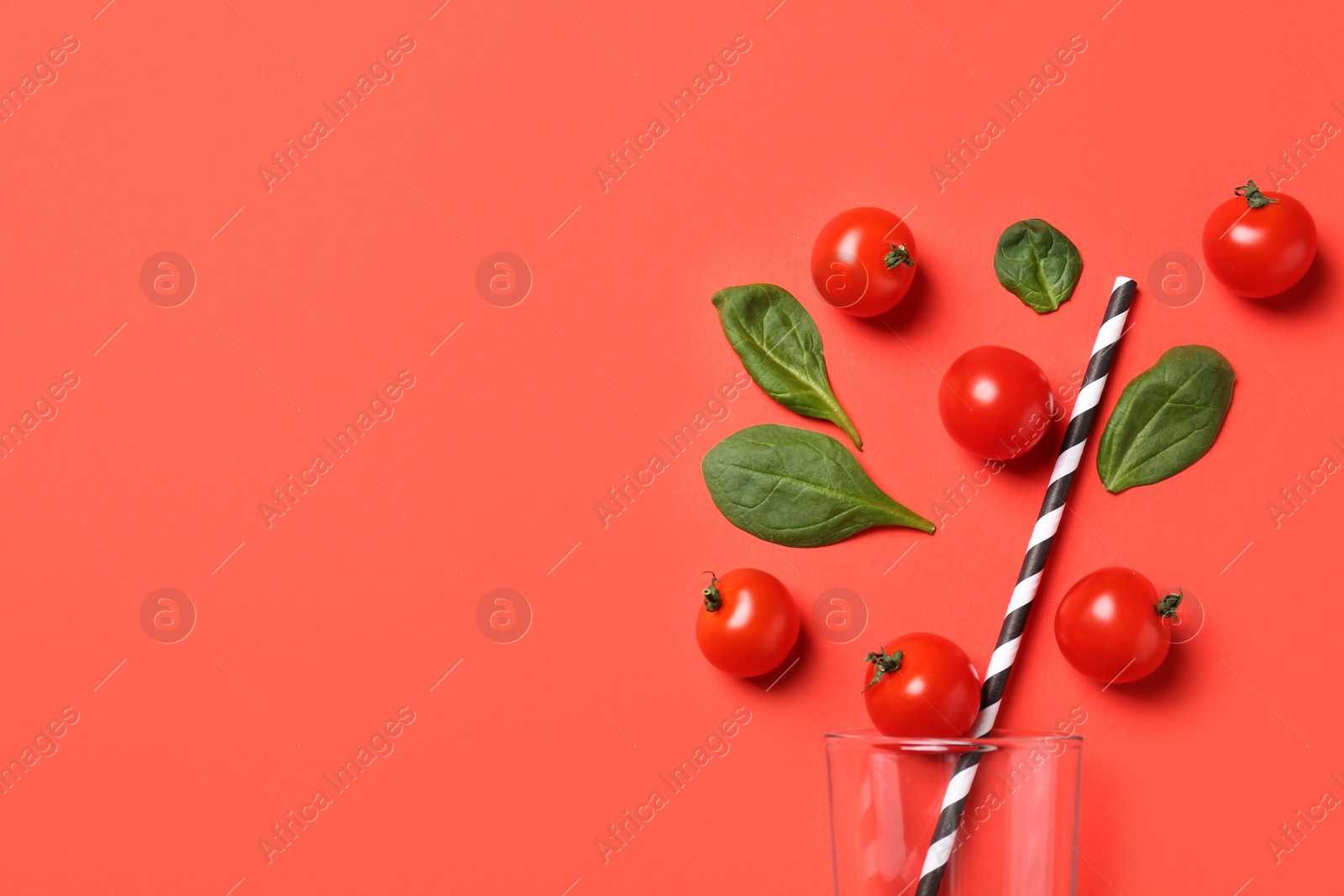 Photo of Cherry tomatoes, spinach leaves and glass with straw on coral background, flat lay. Space for text