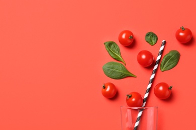 Photo of Cherry tomatoes, spinach leaves and glass with straw on coral background, flat lay. Space for text