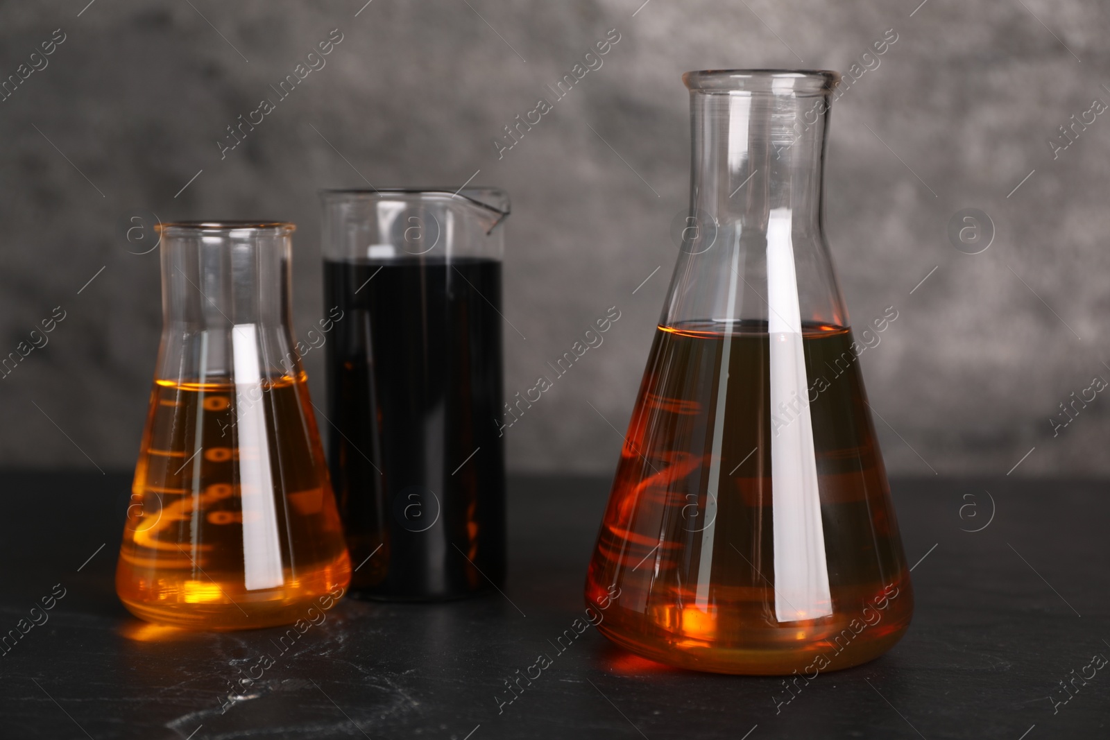 Photo of Beaker and flasks with different types of oil on grey textured table