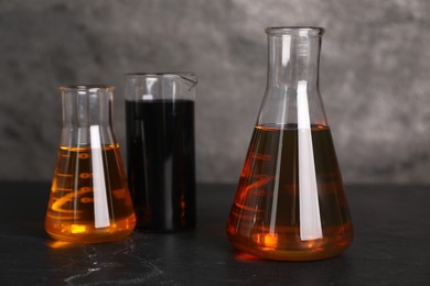 Photo of Beaker and flasks with different types of oil on grey textured table