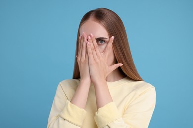 Photo of Embarrassed woman covering face with hands on light blue background