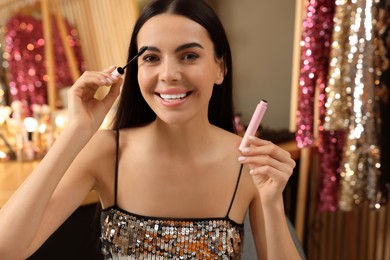 Photo of Beautiful young woman applying mascara in dressing room